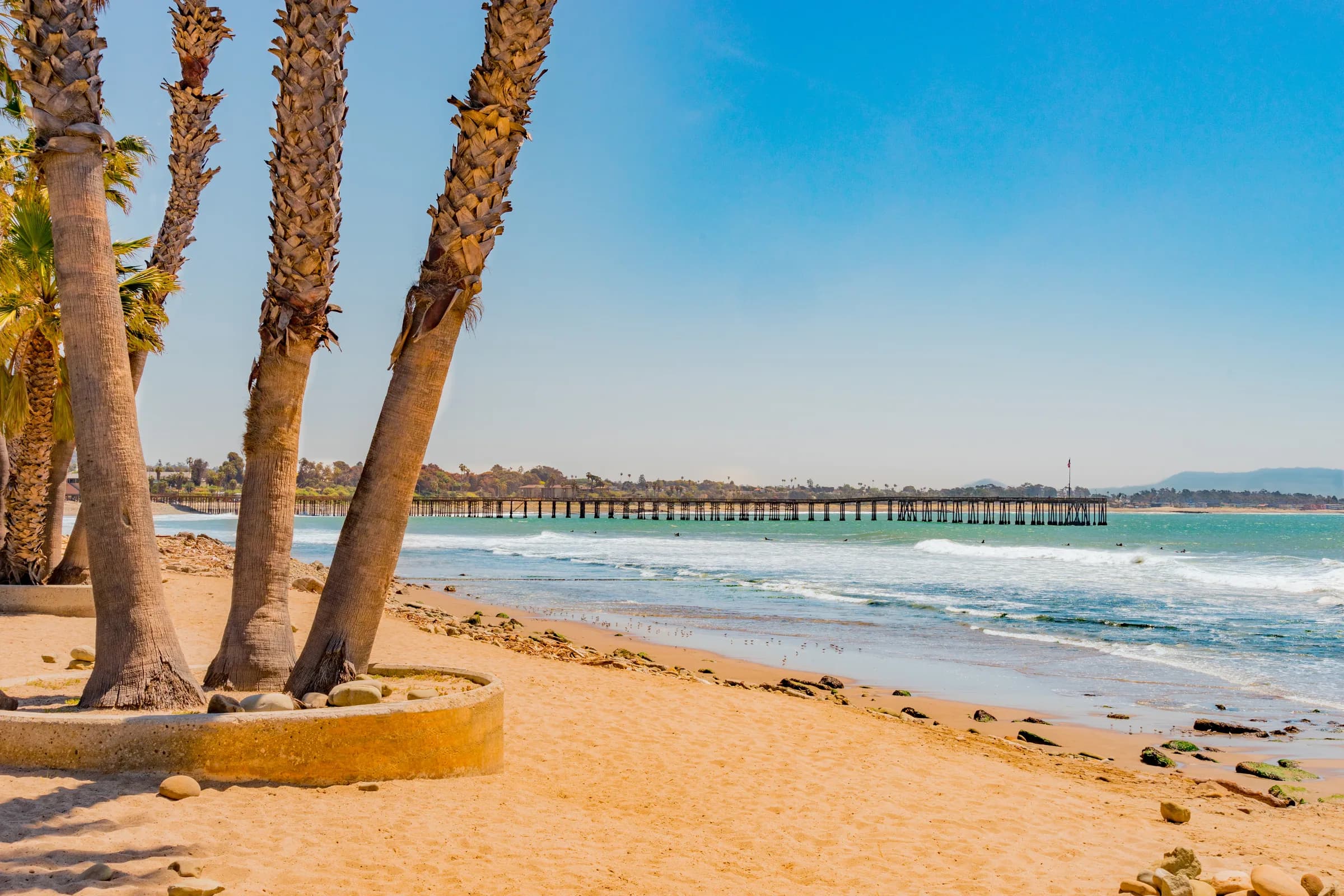 Ventura Pier framed by palm trees on the beach, with the Pacific and coastal mountains in the distance