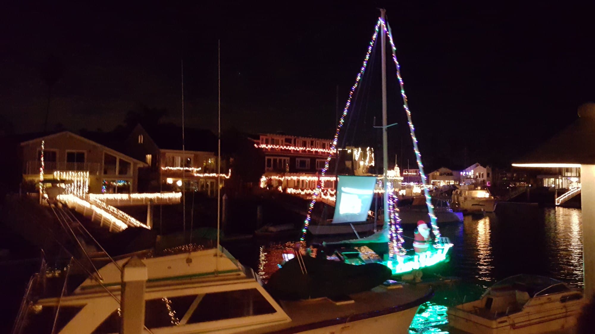 A sailboat strung with Christmas lights, with a Santa on deck, in a Ventura marina on a December night