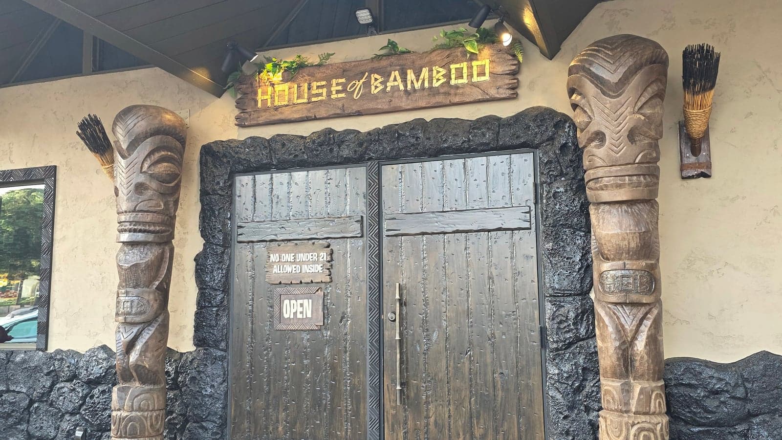 Entrance to House of Bamboo in Old Town Camarillo, with two full-height hand-carved tiki totems flanking lava-rock-framed wooden double doors and a carved HOUSE OF BAMBOO sign above