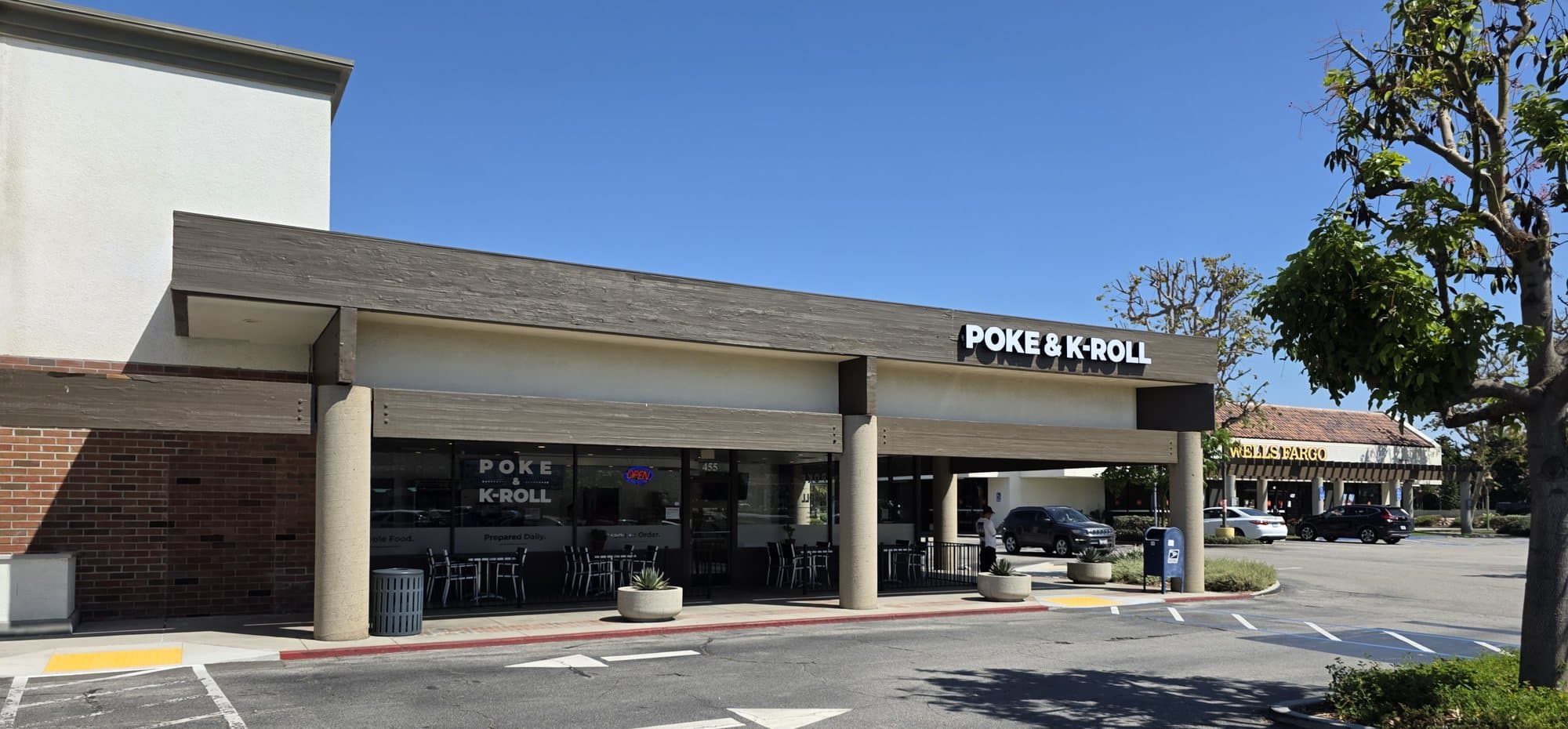 The Poke & K-Roll sign over its storefront in Carmen Plaza on Carmen Drive in Camarillo, with patio tables under the covered walkway