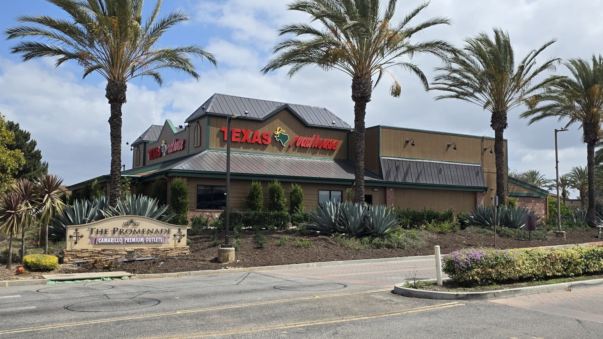 The new Texas Roadhouse in Camarillo behind palm trees and The Promenade at Camarillo Premium Outlets sign
