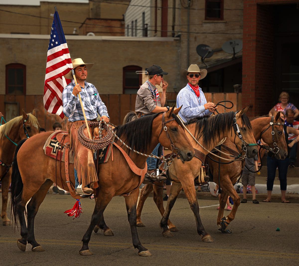 Riders on horseback carrying an American flag in a small-town Independence Day parade