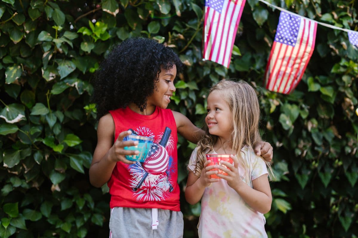Two children waving small American flags outdoors on the Fourth of July