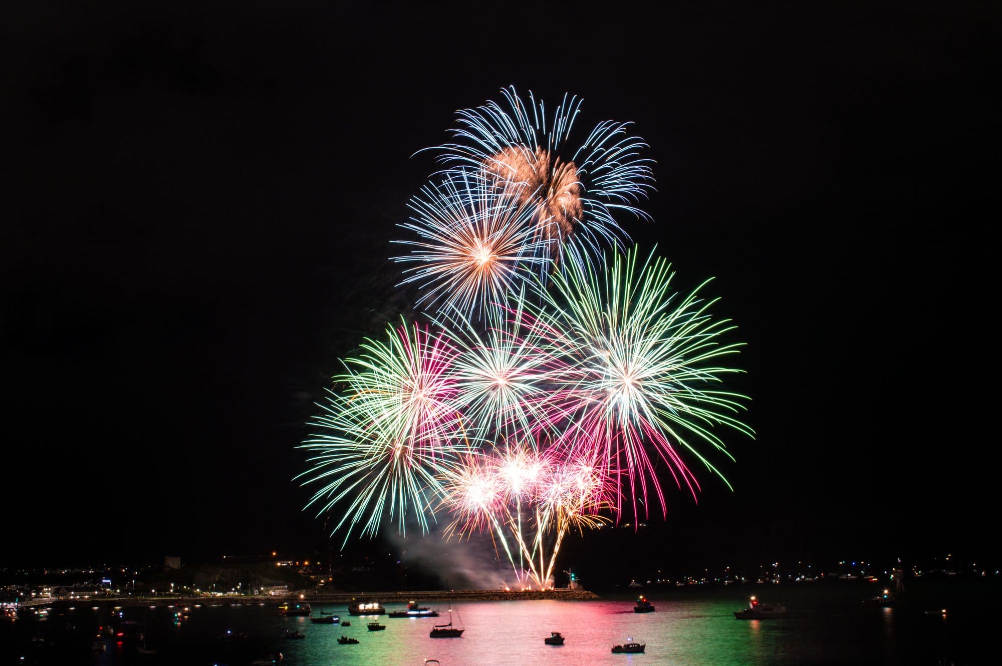 Colorful Fourth of July fireworks bursting over a harbor full of boats on the California coast