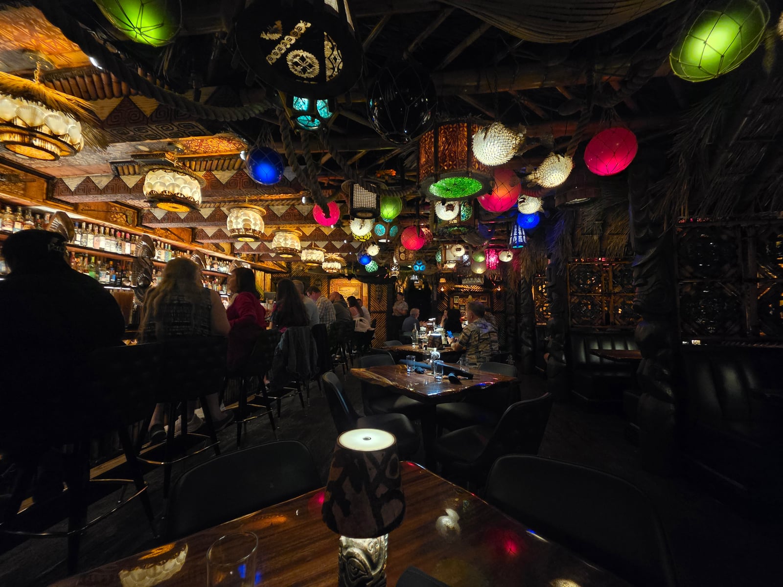 The main bar room at House of Bamboo, with dozens of colored paper lanterns hung from the ceiling, dark wood booth seating, and an intimate Polynesian-themed interior