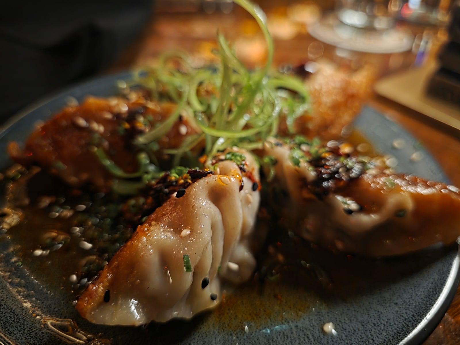 Pan-Fried Dumplings at House of Bamboo, crescent-shaped house-made pork and bamboo dumplings on a dark plate with ponzu, chili oil, and sliced scallions