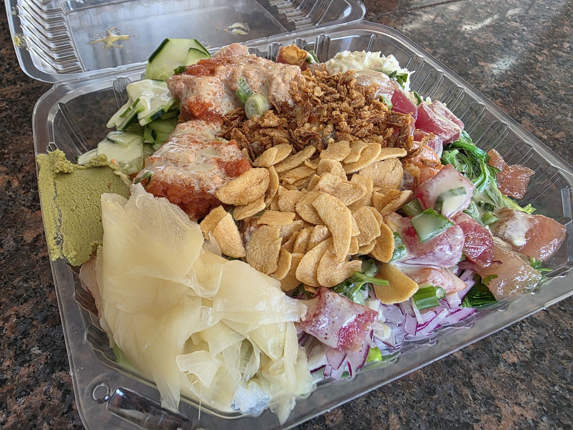 A four-scoop poke bowl from Poke & K-Roll in Camarillo in a clear takeout container, with spicy tuna, raw tuna, salmon and albacore, crabmeat, seaweed, crispy garlic, crispy onion, ginger, wasabi and cucumber