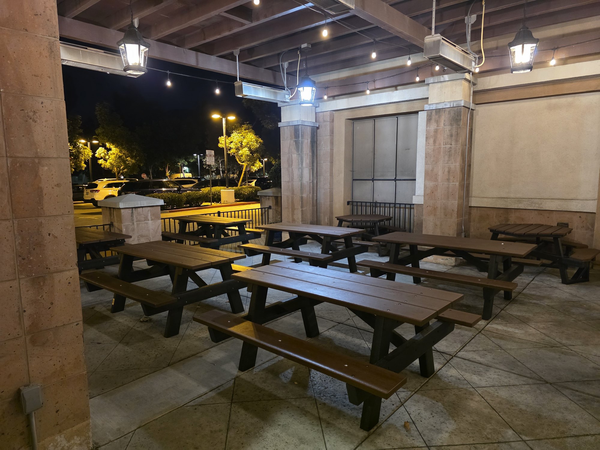 The covered outdoor patio at Snapper Jack's Taco Shack in Camarillo at night, with rows of dark wood picnic tables under hanging lamps