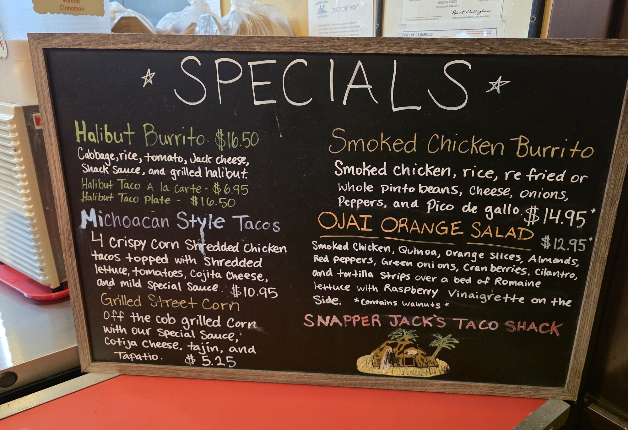 The handwritten specials chalkboard at Snapper Jack's Taco Shack in Camarillo listing the halibut burrito, Michoacan style tacos, grilled street corn, smoked chicken burrito and Ojai orange salad with prices