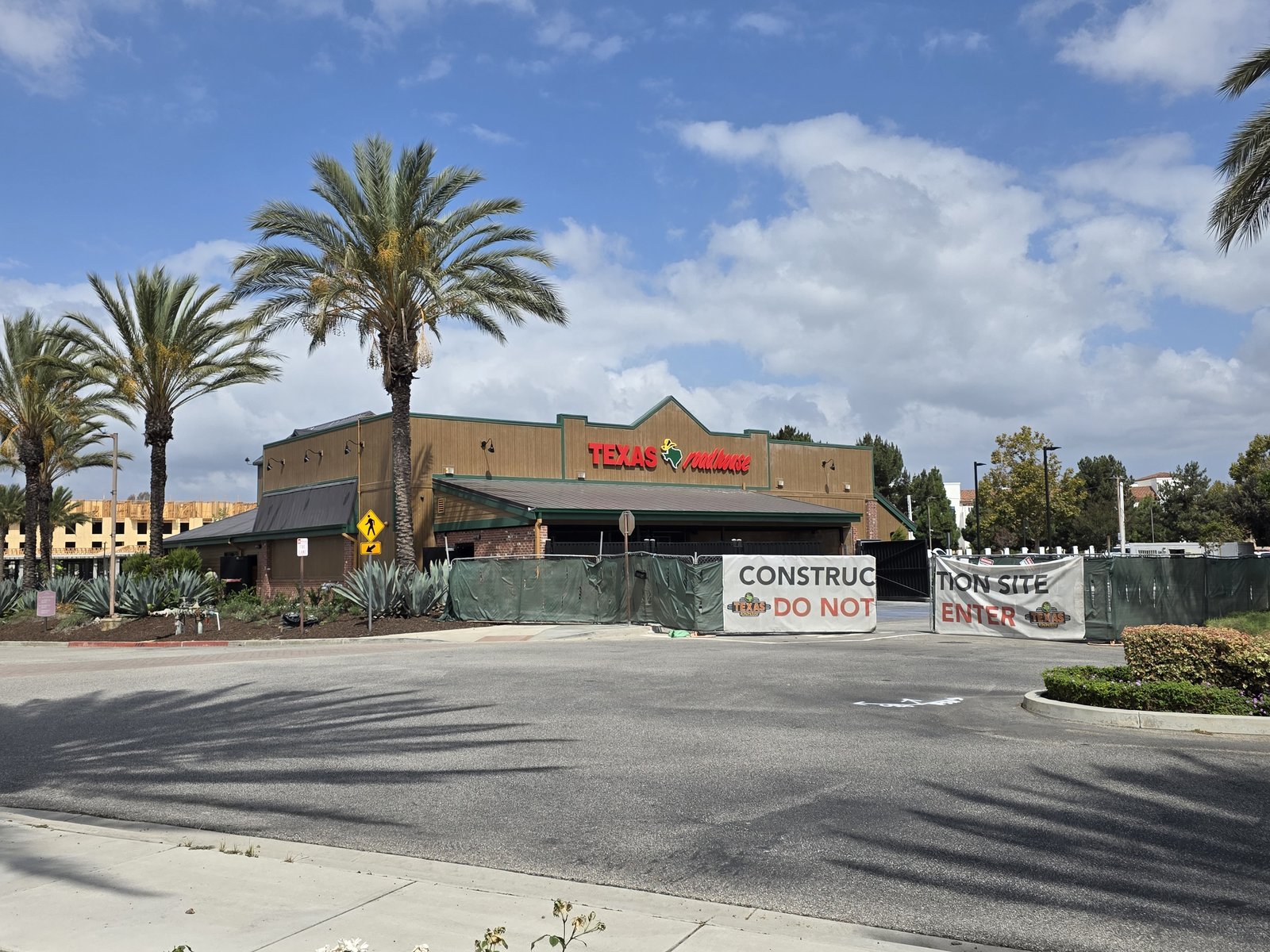 The Texas Roadhouse building in Camarillo behind a construction fence with Construction Site Do Not Enter signs and palm trees